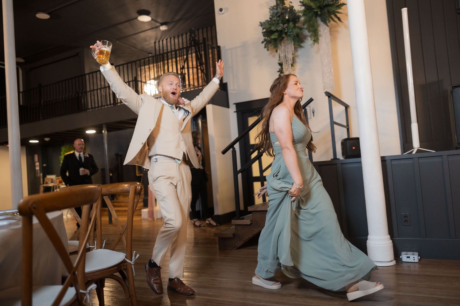 Wedding party dancing and celebrating at indoor reception with exposed brick walls and decorative lighting.