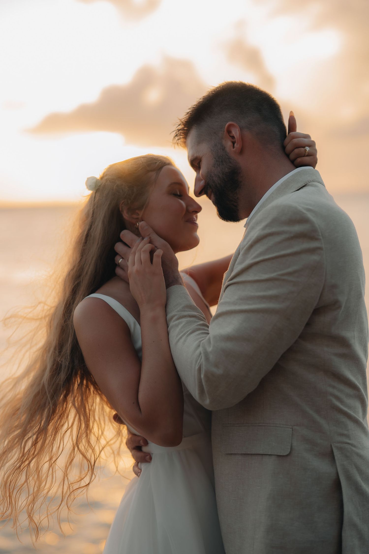 Romantic sunset beach photoshoot of couple embracing in formal attire.
