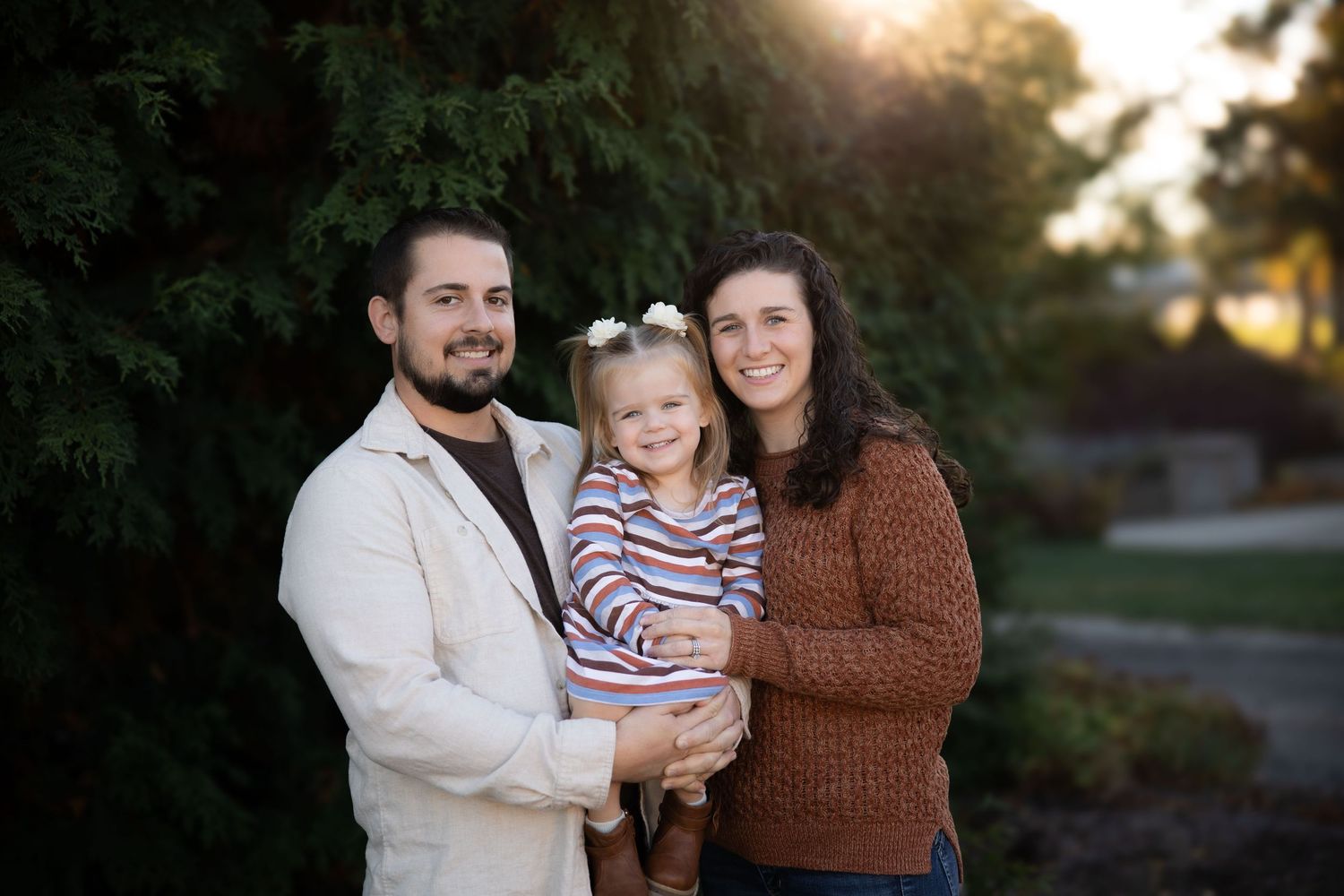 Family of three poses together at sunset in autumn setting.