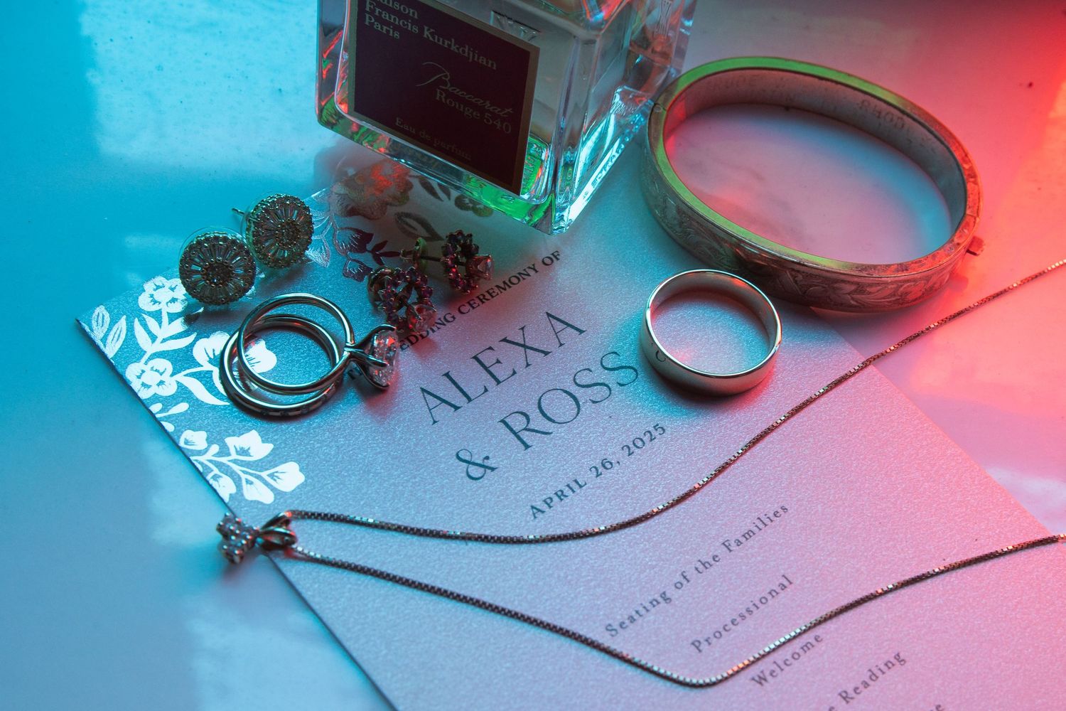Wedding rings and invitation details photographed with dramatic blue and red lighting effects.