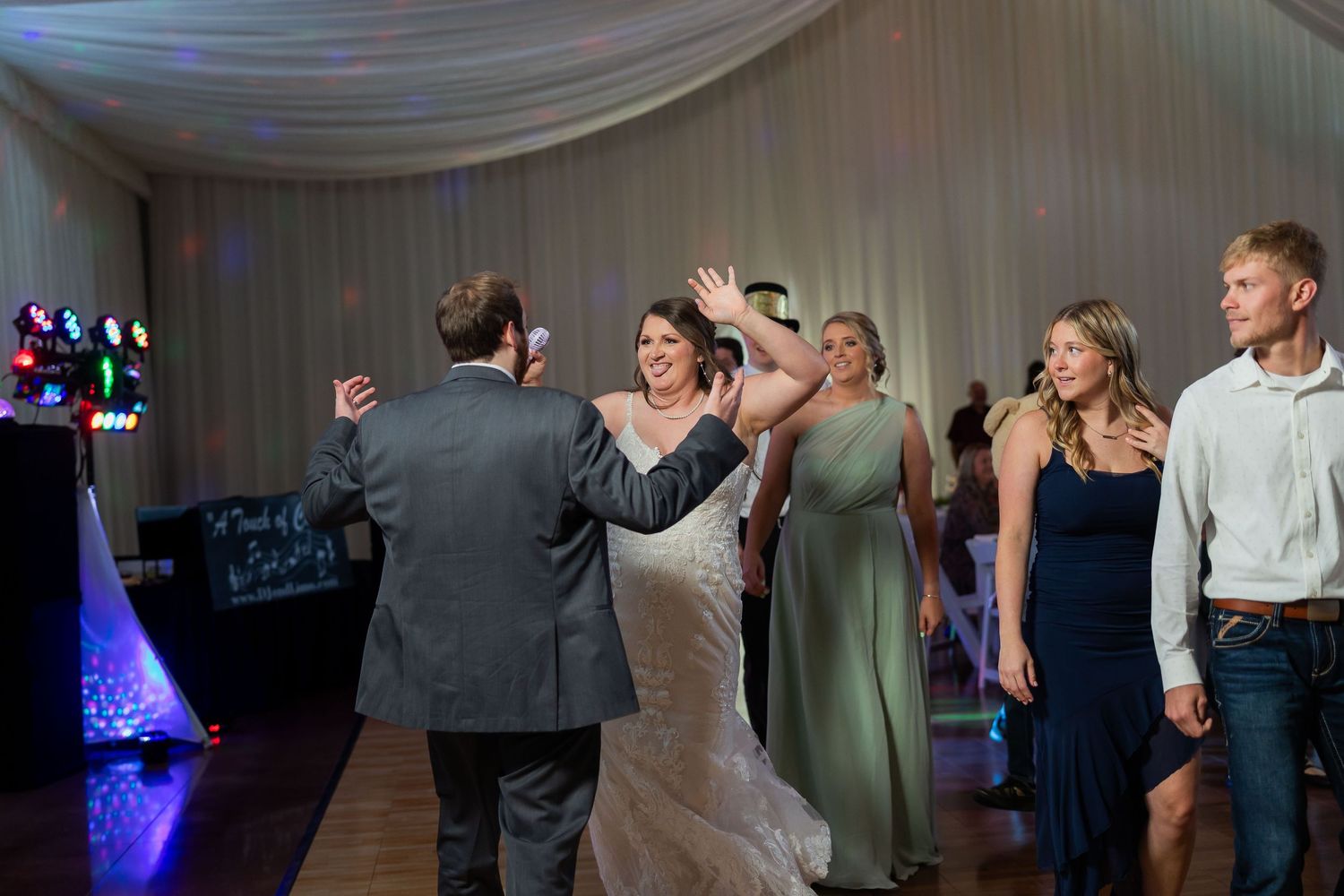 Bride and groom share first dance at elegant wedding reception with guests celebrating in background.