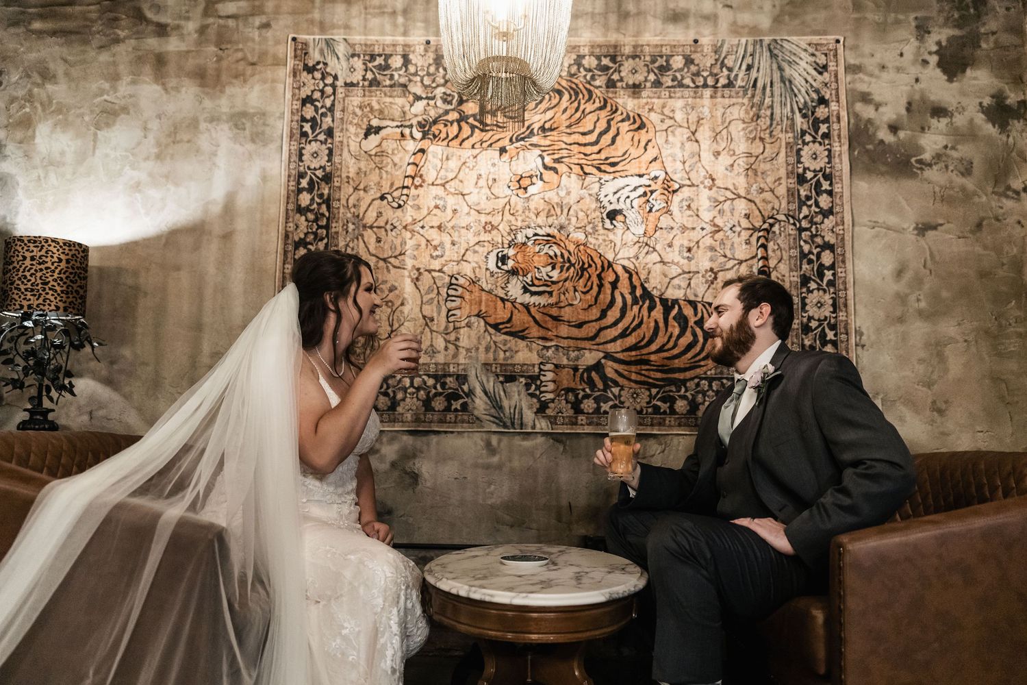 Bride and groom toasting with champagne in front of a ornate tiger tapestry at their wedding reception.