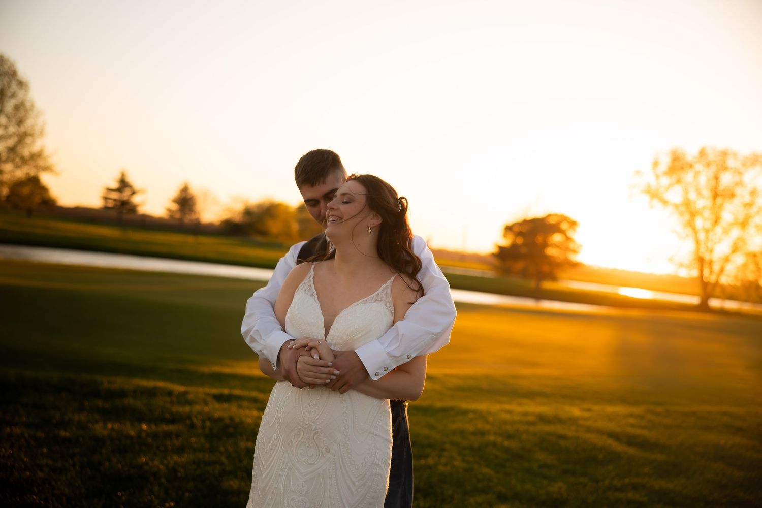 Couple embraces romantically at golden sunset on lush green lawn.