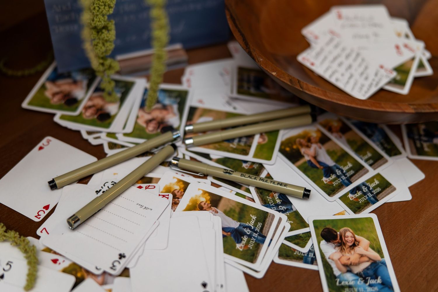 Custom playing cards with couple photos scattered on table with pens as wedding reception decor.