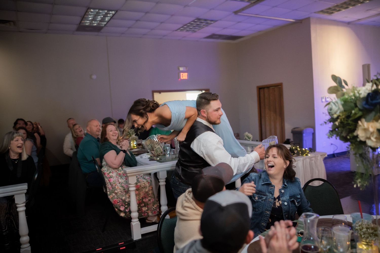 Wedding guests laugh and celebrate as bride and groom interact during lively reception party.