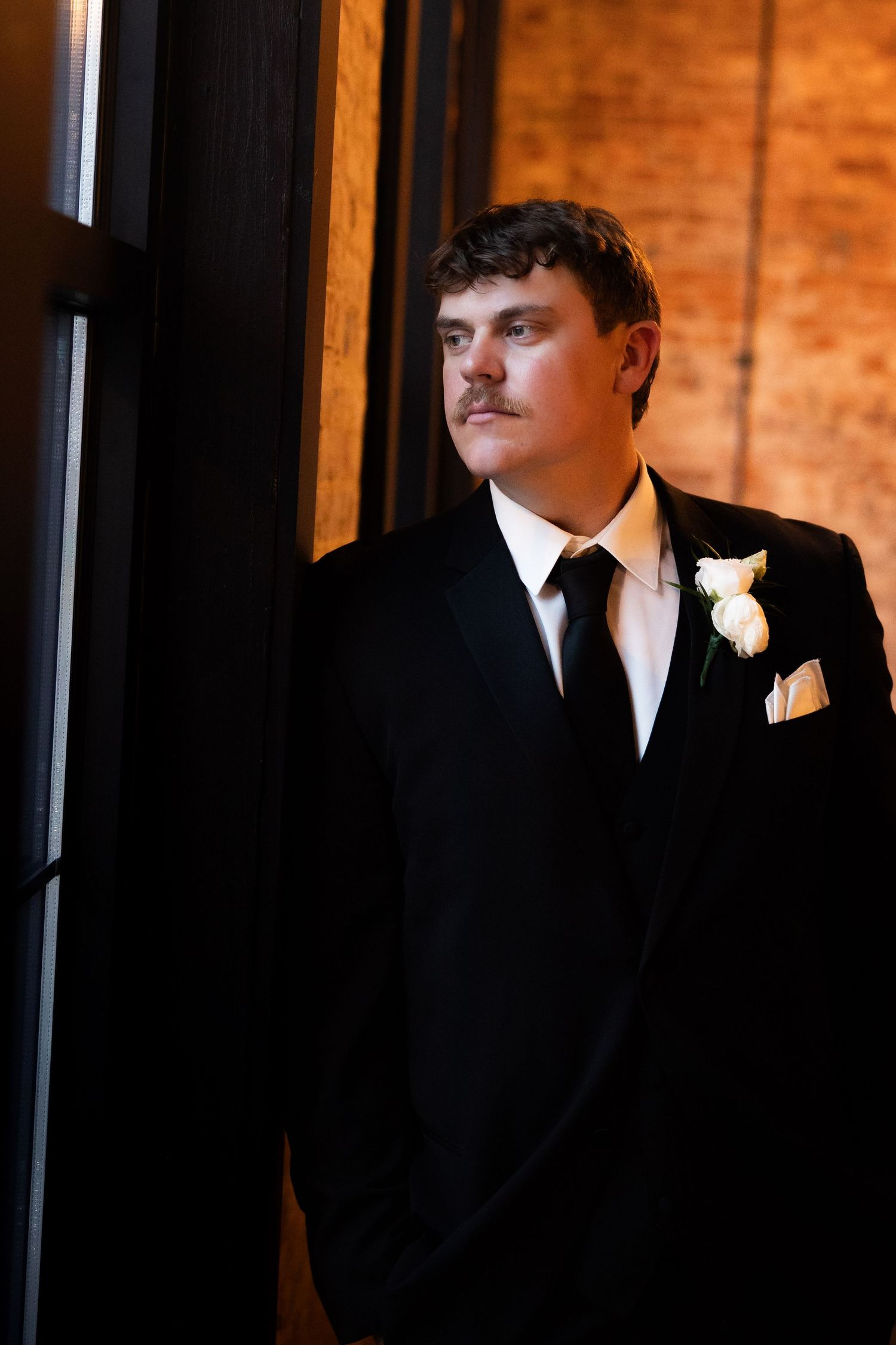 Groomsmen in black suits with white boutonnieres against dark background.