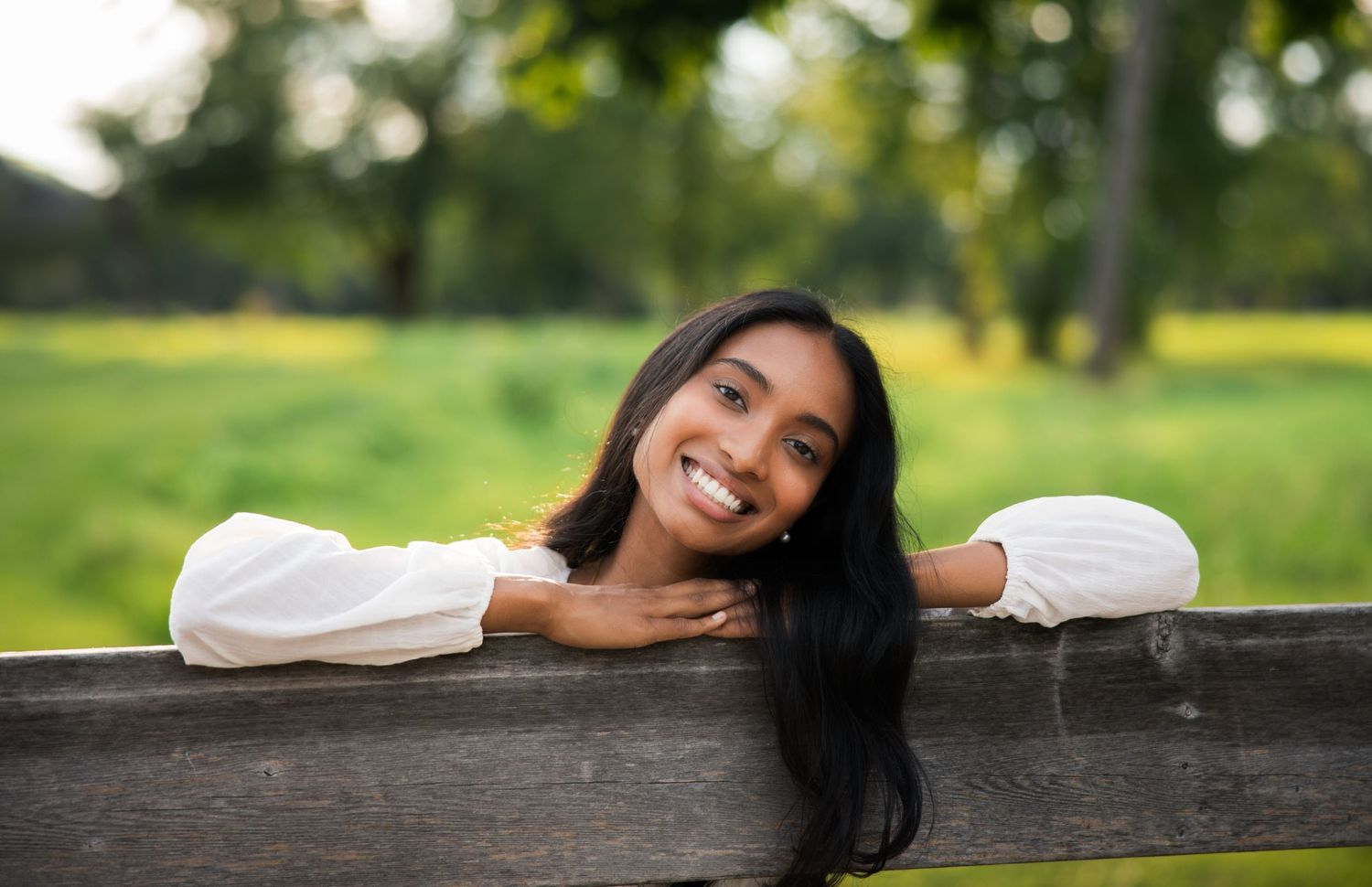 Person resting on wooden fence with natural greenery in background.