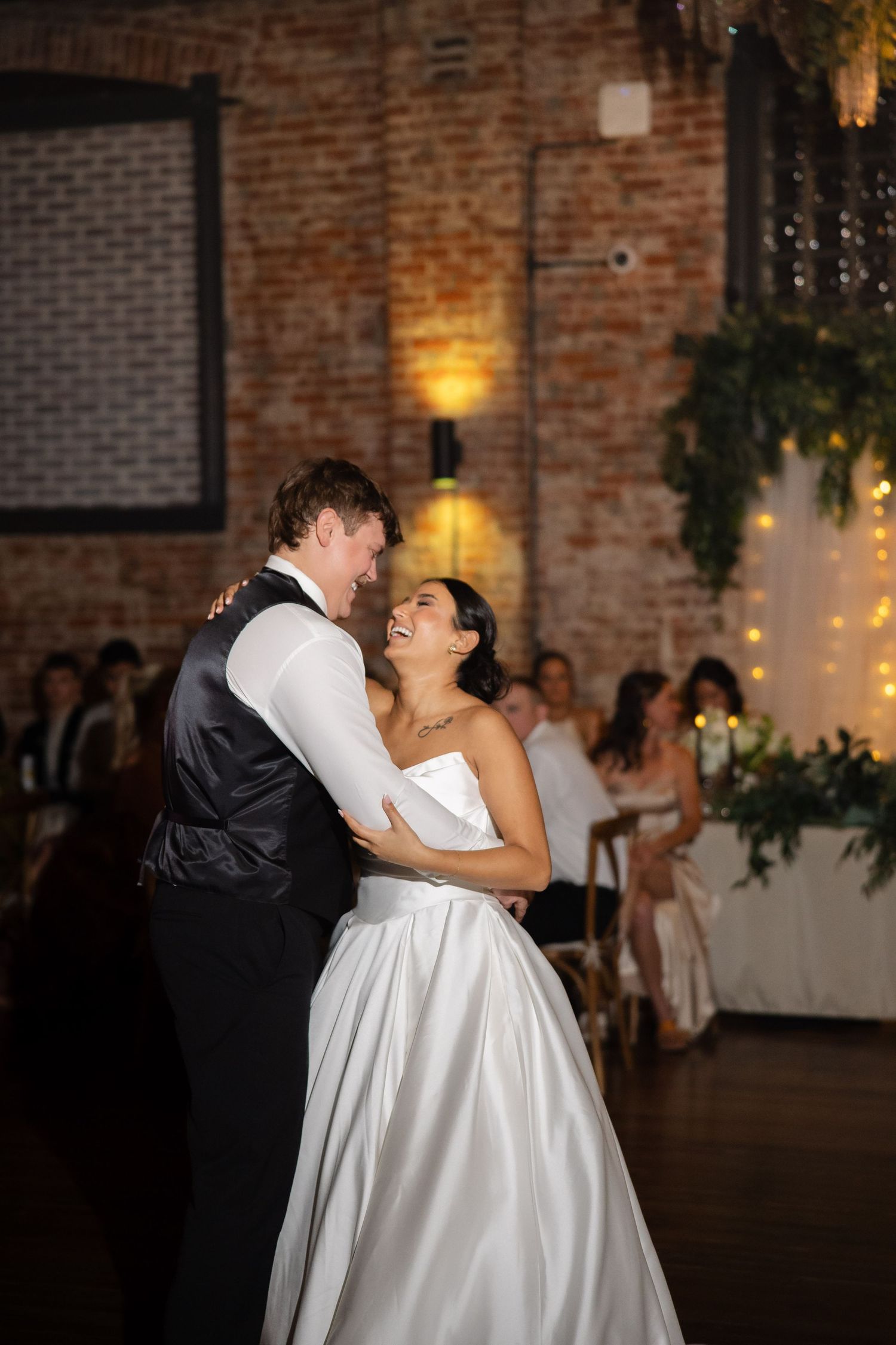 Newlyweds performing romantic dip during their first dance in rustic brick venue.