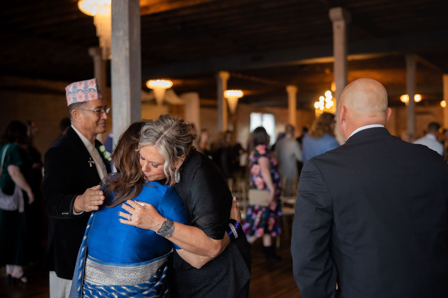 Wedding guests embrace and celebrate during an emotional reception moment in an industrial-style venue.