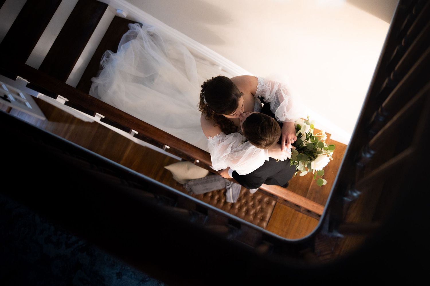 Aerial view of bride and groom sharing a tender moment on wooden stairs, bride in white gown holding bouquet.