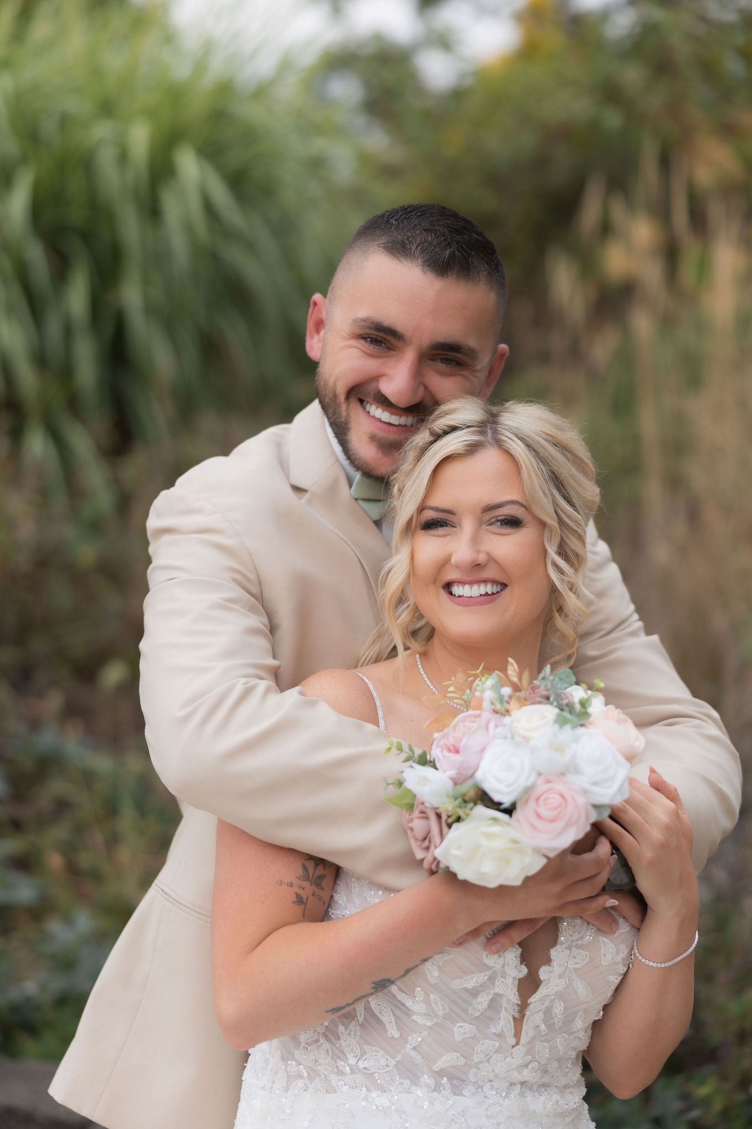 Romantic wedding portrait with couple holding bouquet of pink and white roses in garden setting.