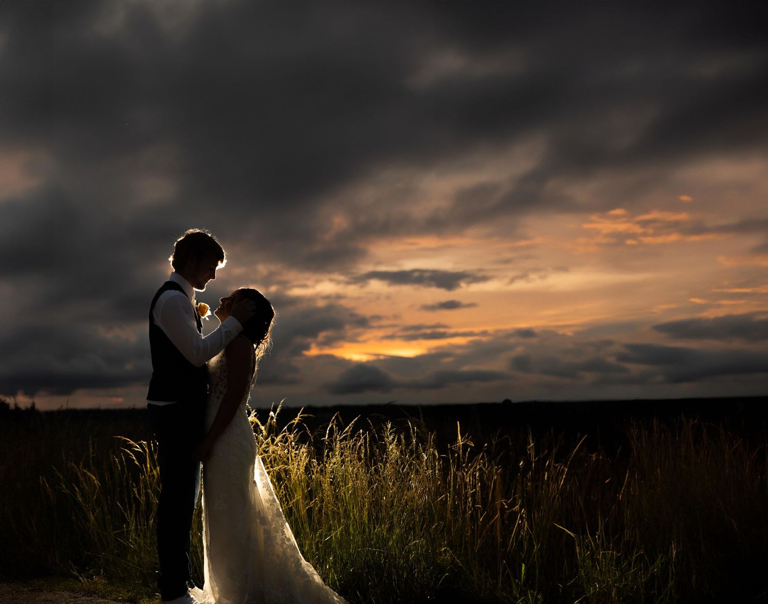 Dramatic sunset silhouettes couple in wedding attire against golden sky.