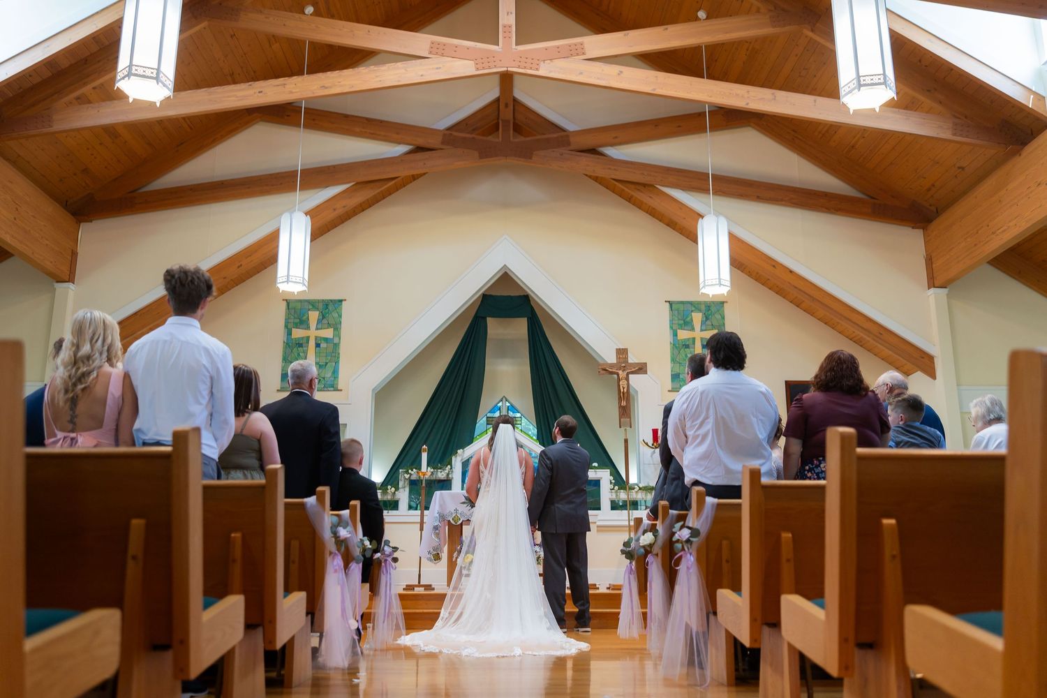 Wedding ceremony in a wooden chapel with bride and groom at the altar, guests seated in pews.