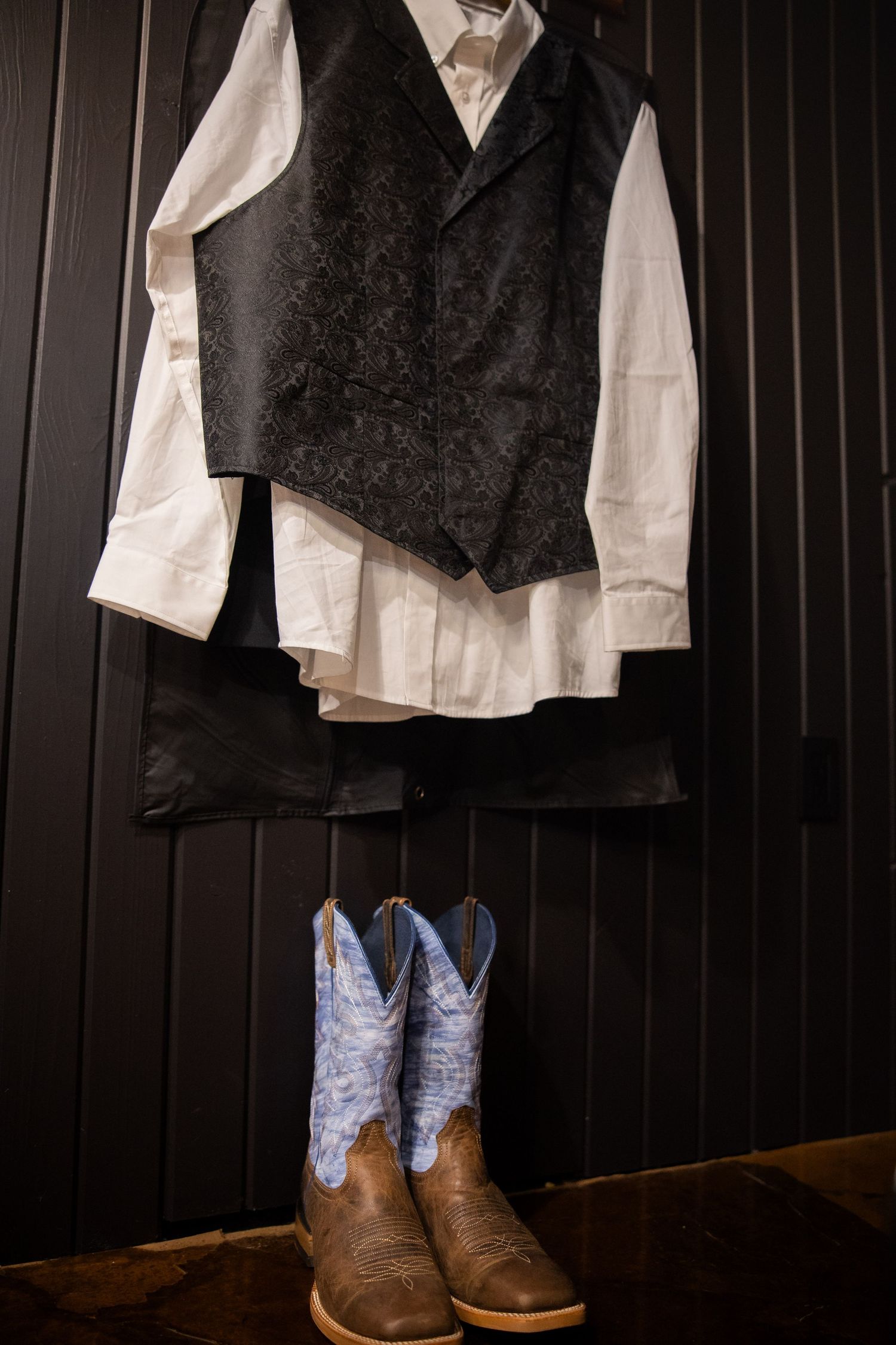 Men's formal attire including white dress shirts, black vests, and brown leather boots displayed against dark paneling.