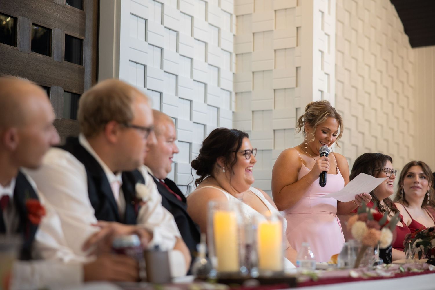 Wedding reception guests seated at tables along a textured white wall.