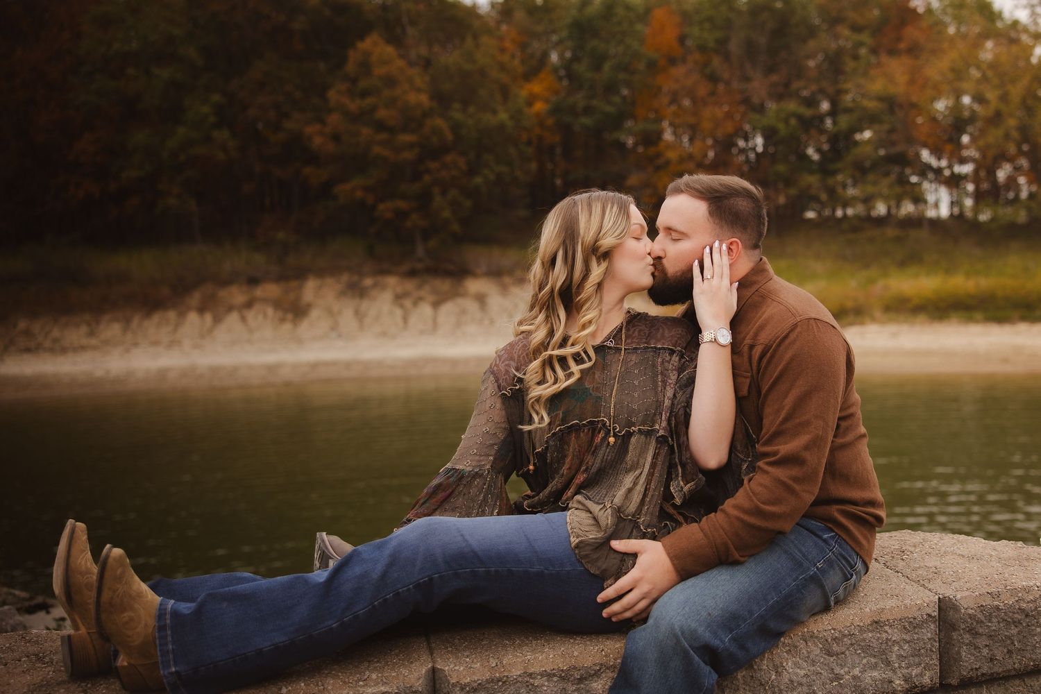 A couple shares romantic moments in autumn scenery by a lake during golden hour.