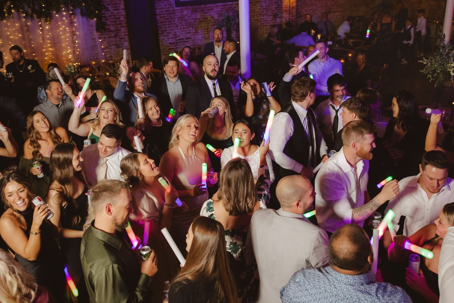 Wedding reception dance floor filled with guests enjoying the celebration under purple lighting.