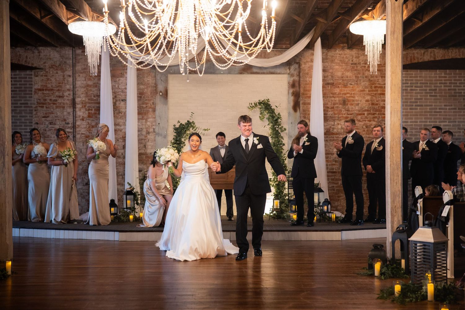 Wedding reception in an elegant brick venue with chandeliers and guests gathered.