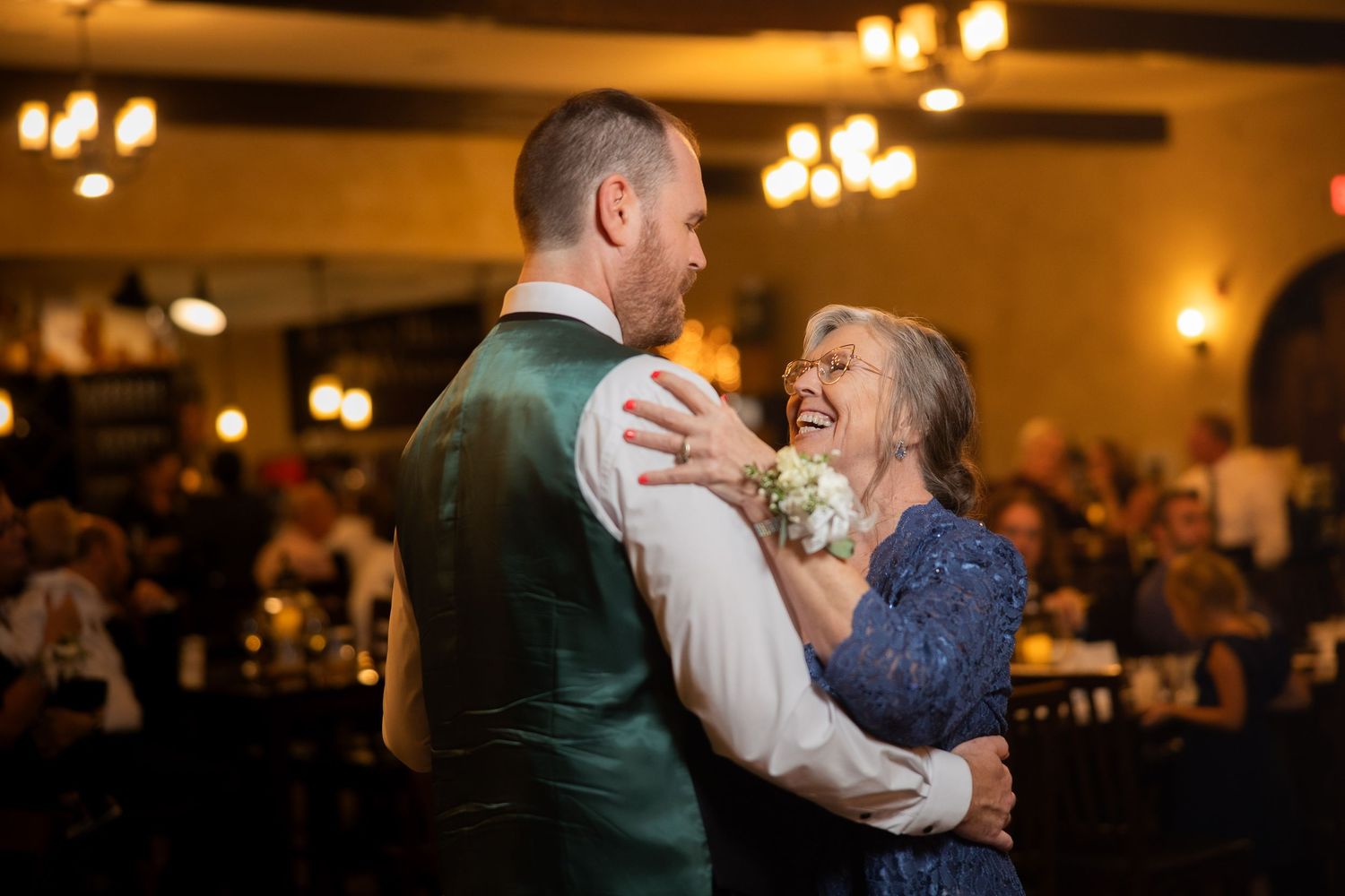 A couple dances together at their wedding reception in a warmly lit ballroom.