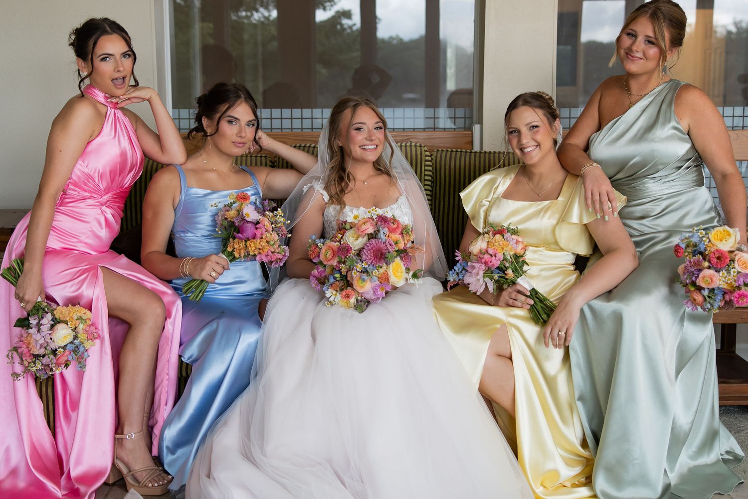 Bride in white gown poses with four bridesmaids in colorful pastel dresses holding vibrant bouquets.
