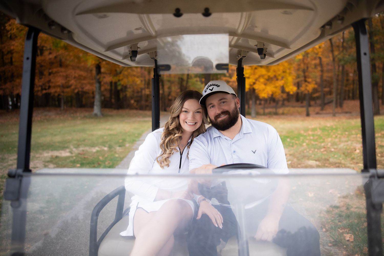 Happy couple rides in a golf cart together during autumn with colorful fall foliage in the background.