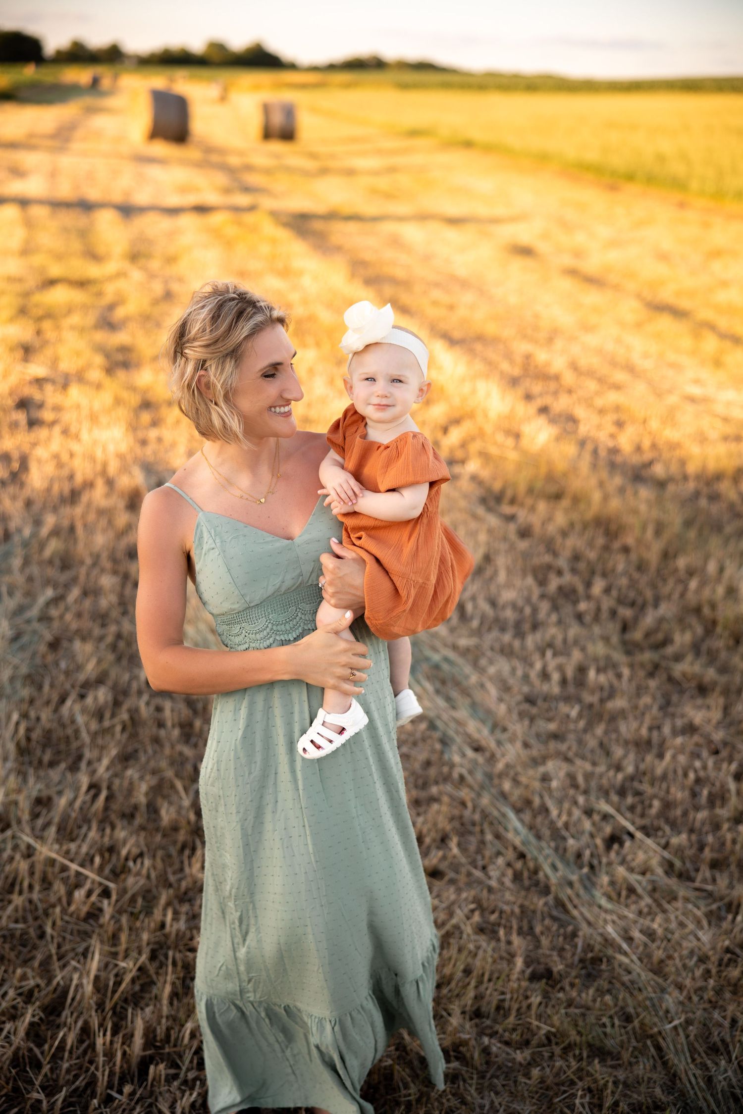 Mother and baby portrait session in a golden wheat field at sunset wearing sage green dress.