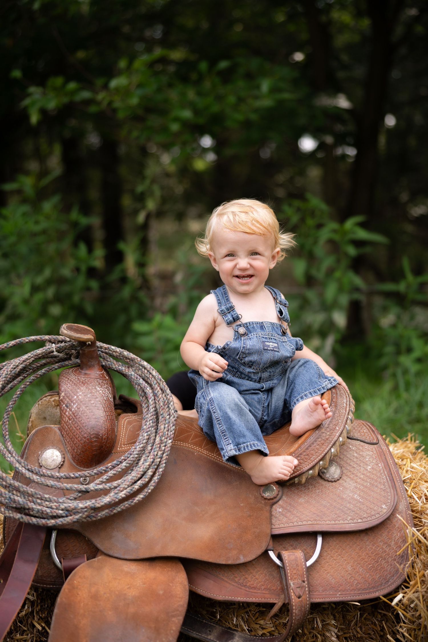 Small child sitting on vintage leather horse saddle in outdoor setting.