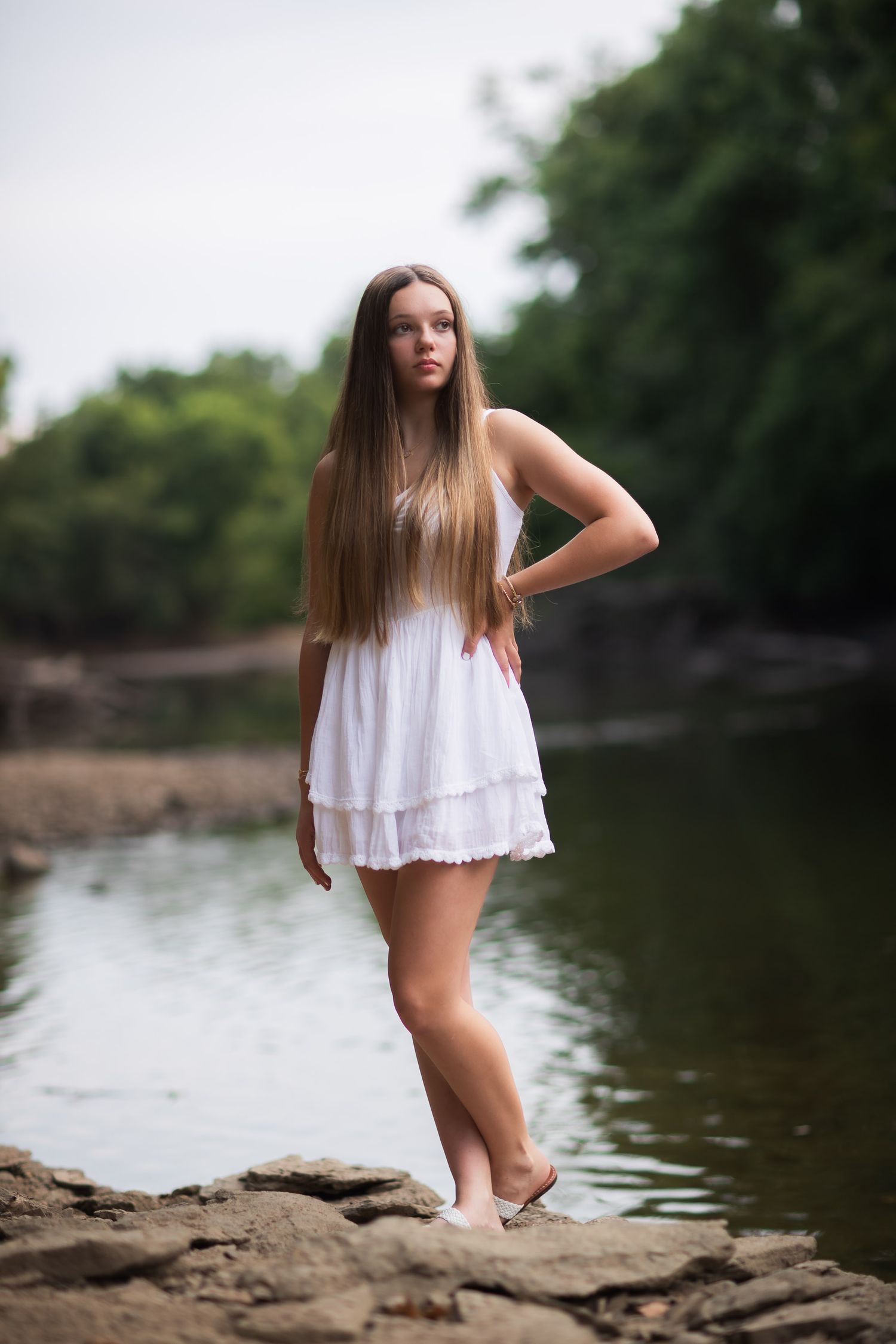 White summer dress portrait by a serene lake with rocky shoreline.