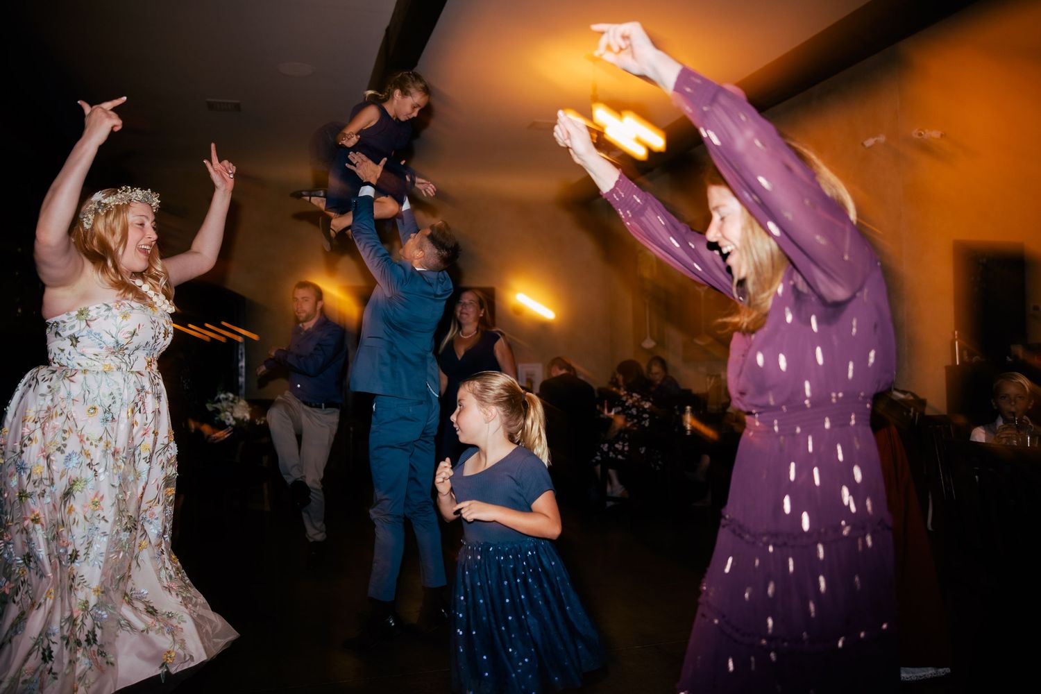 People dancing energetically at a celebration with a purple dress and navy dress visible in the festive atmosphere.