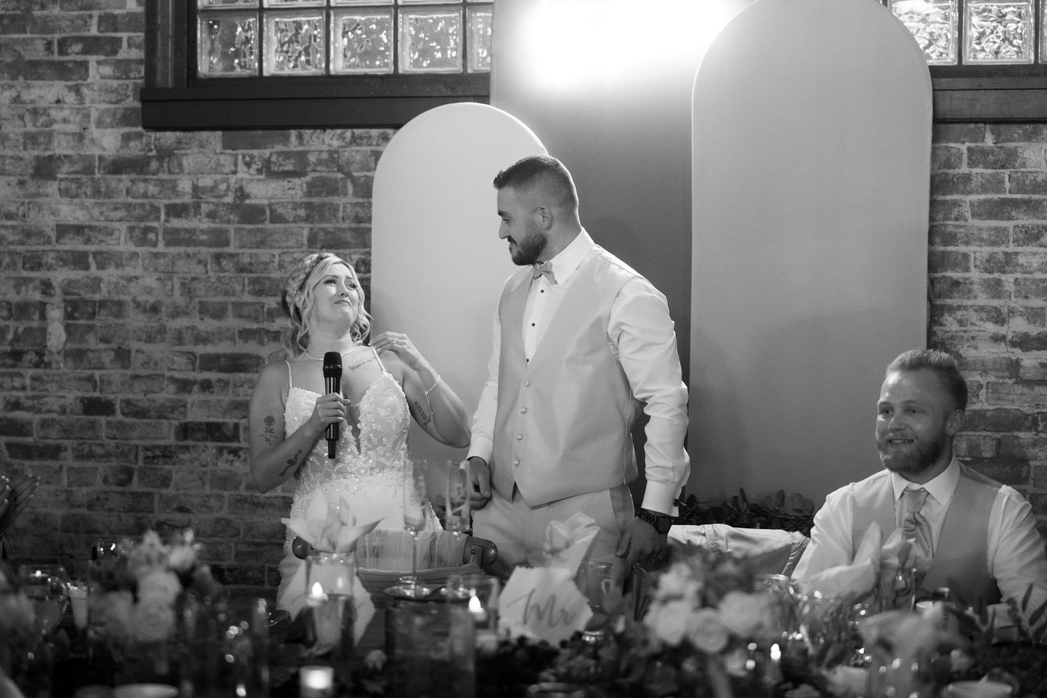 Wedding reception in a brick-walled venue with guests seated at decorated tables.