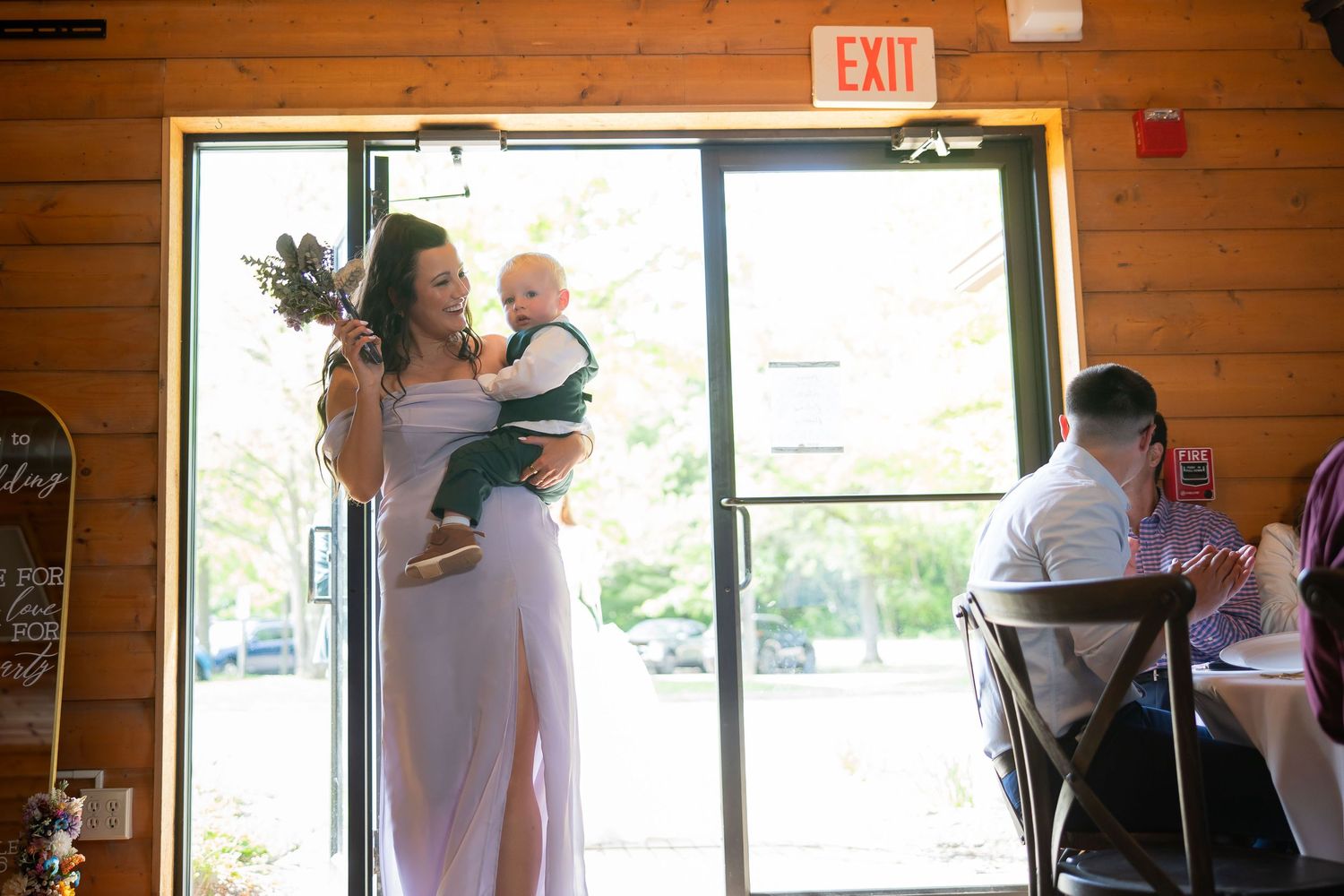 Woman in white dress holding baby near exit door at indoor wedding reception venue.