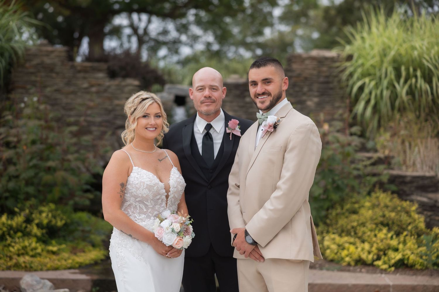 Outdoor wedding portrait taken in front of stone wall and garden landscaping.