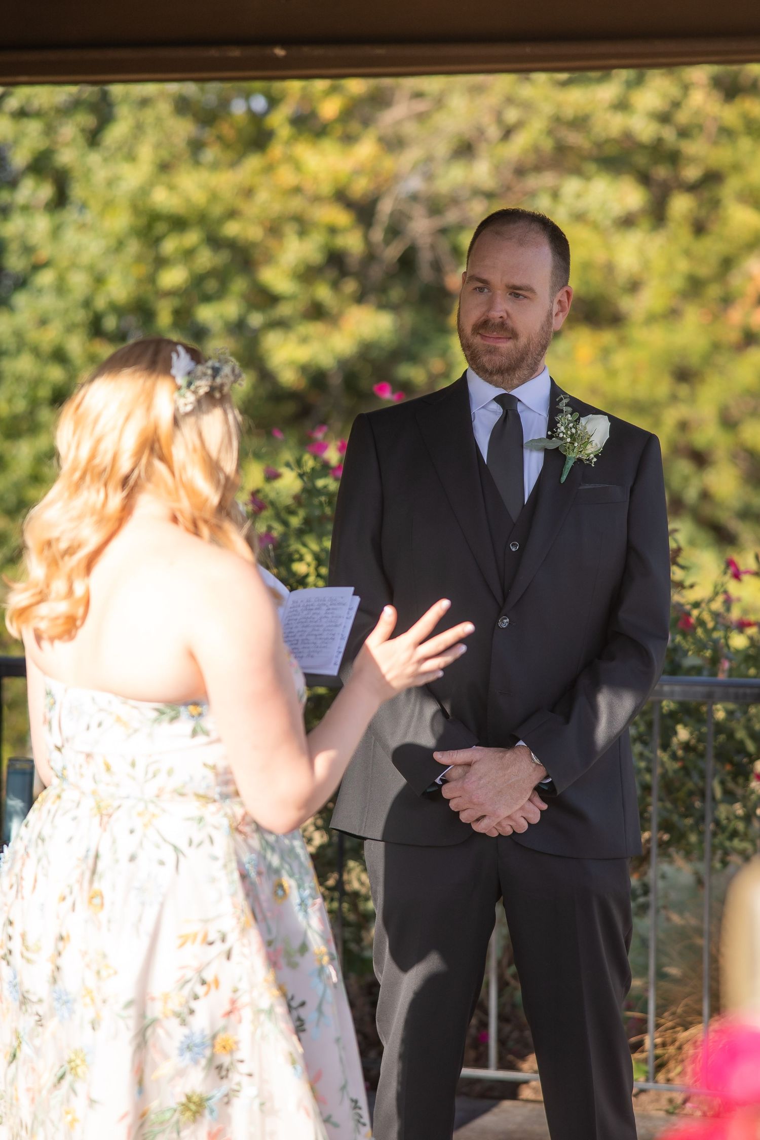 Couple exchanges vows during an outdoor wedding ceremony surrounded by lush gardens and flowers.