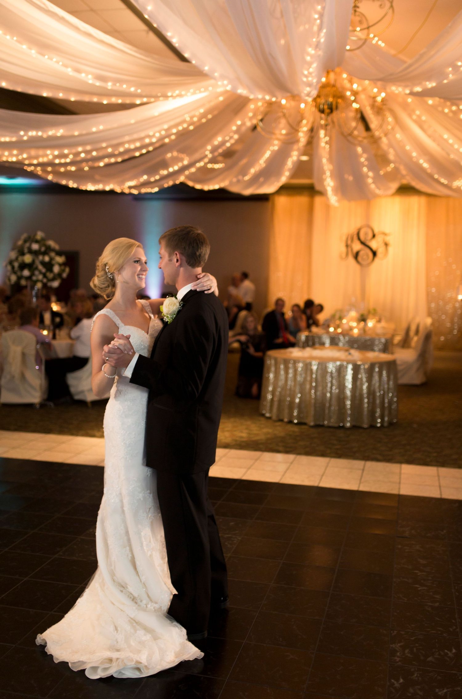 Wedding reception venue decorated with elegant white drapery and twinkling lights.
