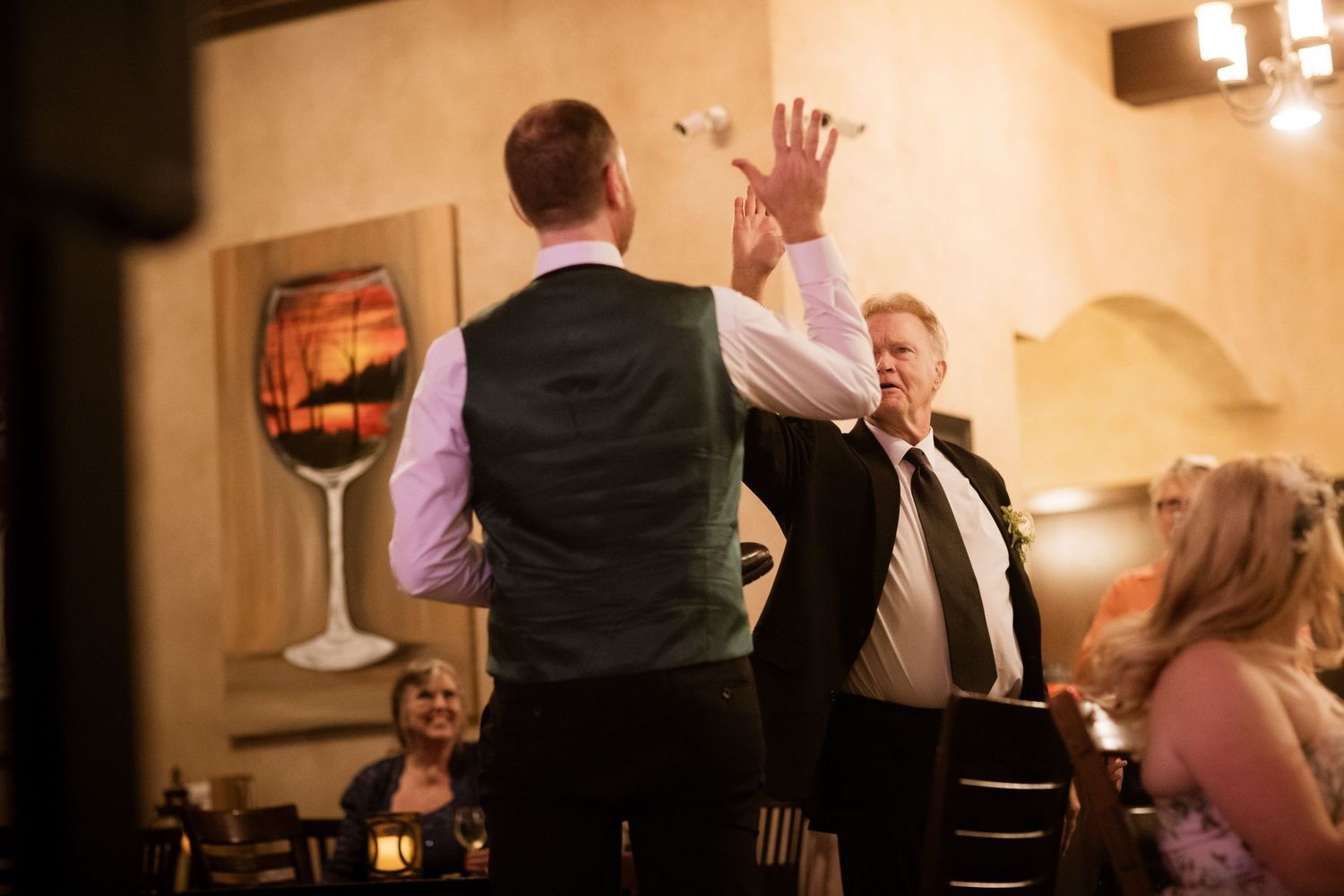 Wedding reception guests dancing and celebrating in a warmly lit indoor venue.
