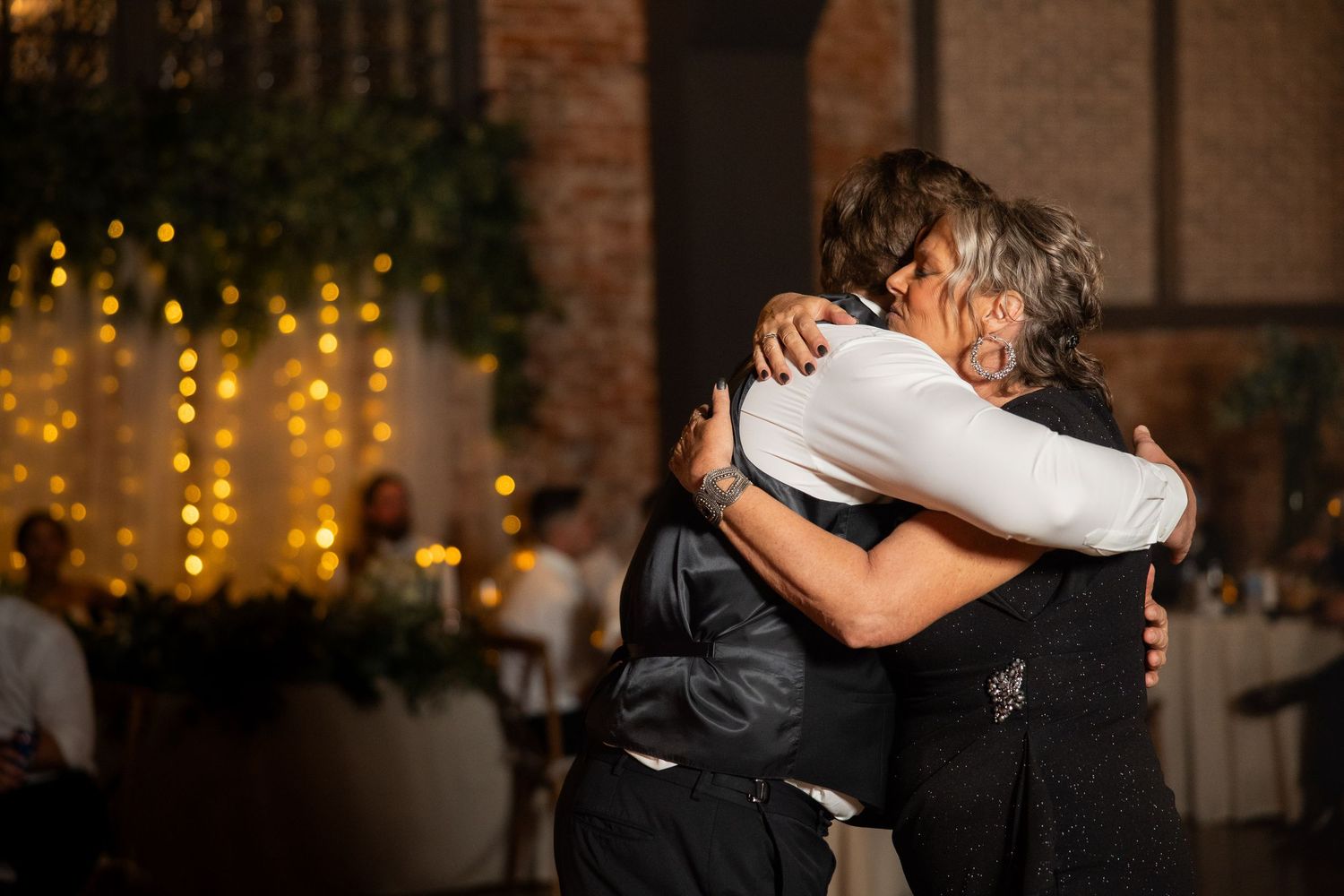 Couple sharing their first dance at wedding reception with string lights in background.