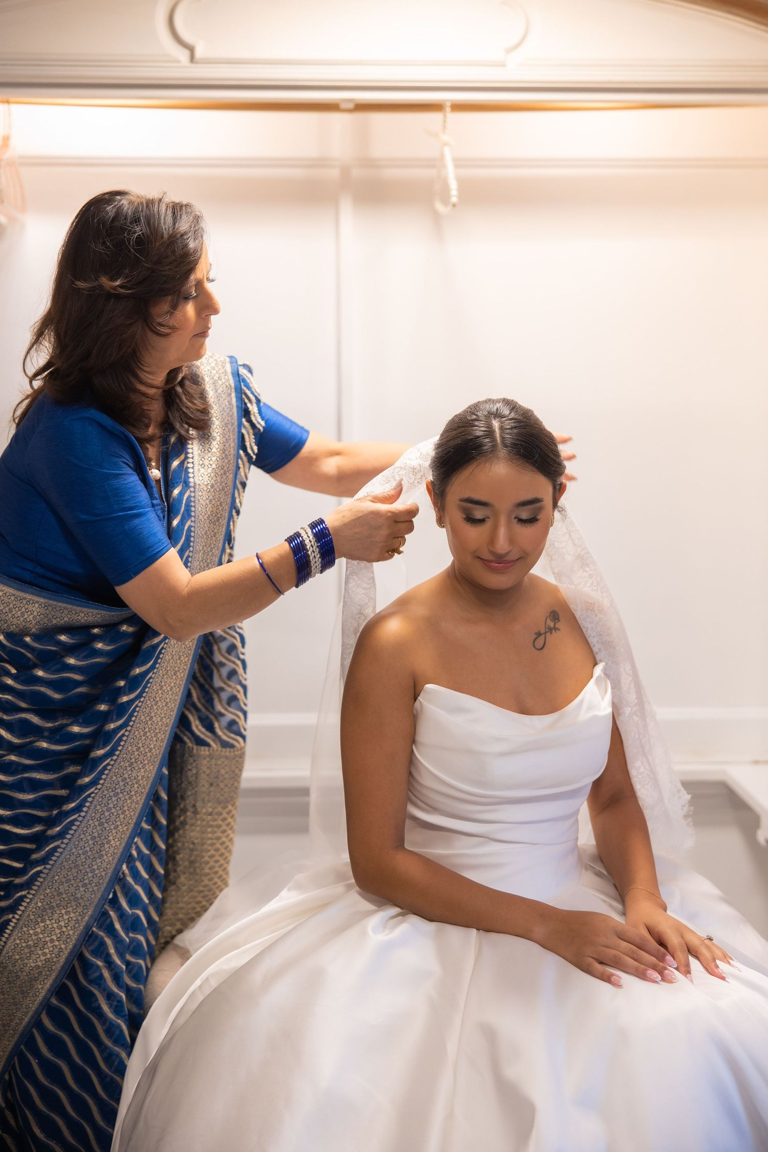 Getting ready scene showing final touches being made to a white wedding dress in a brightly lit room.