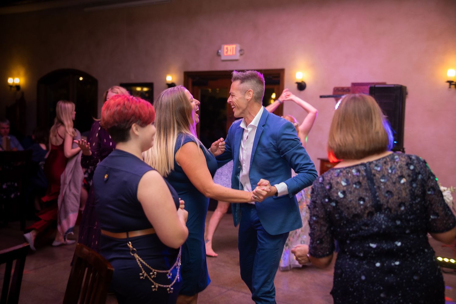 People dancing and celebrating at a wedding reception with pink ambient lighting.