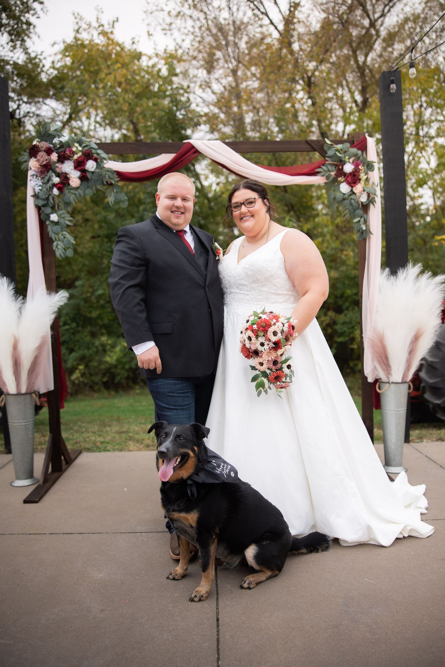 A couple poses with their black and brown Rottweiler dog at their outdoor wedding ceremony.