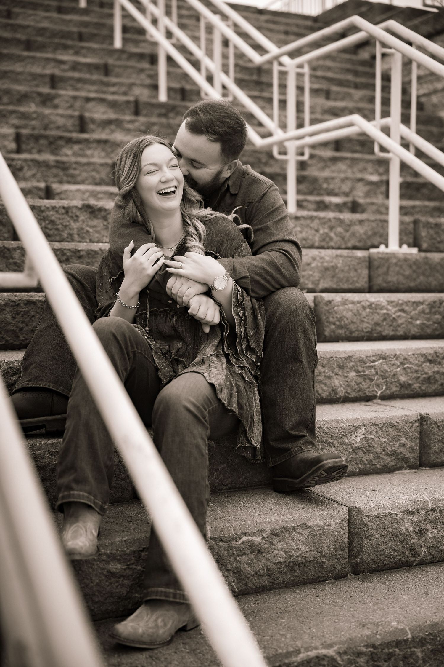 A couple shares a tender moment together while sitting on concrete stadium steps in black and white.