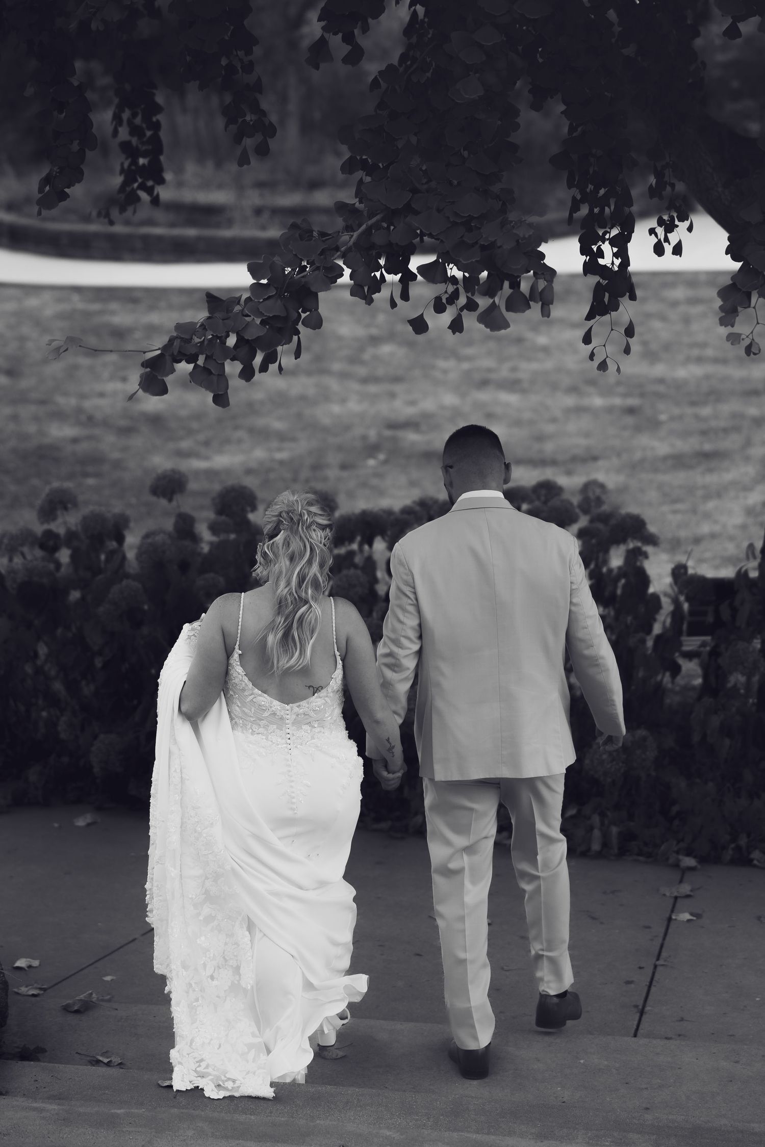 A black and white photo of a couple walking together outdoors, with the bride in a flowing white dress.