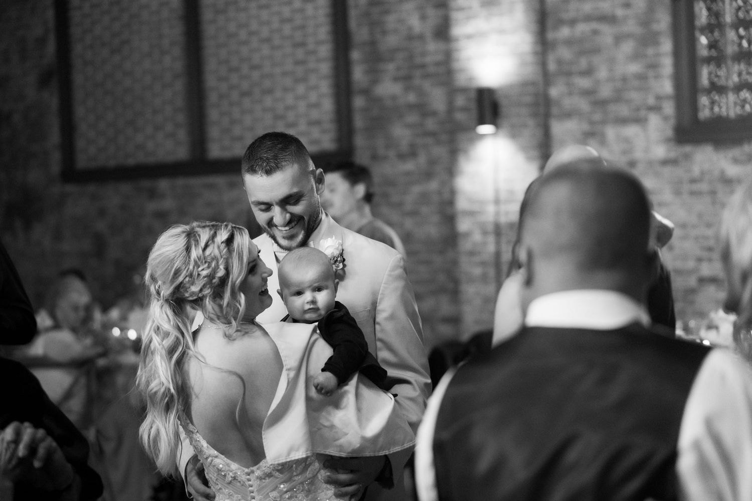 Wedding reception dance floor moments captured in a rustic brick venue with ambient lighting.