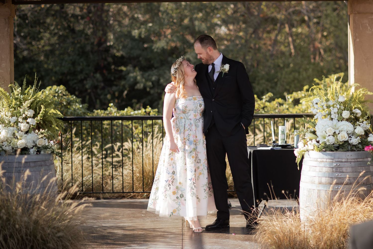 Outdoor wedding ceremony taking place under a rustic wooden pavilion at sunset.