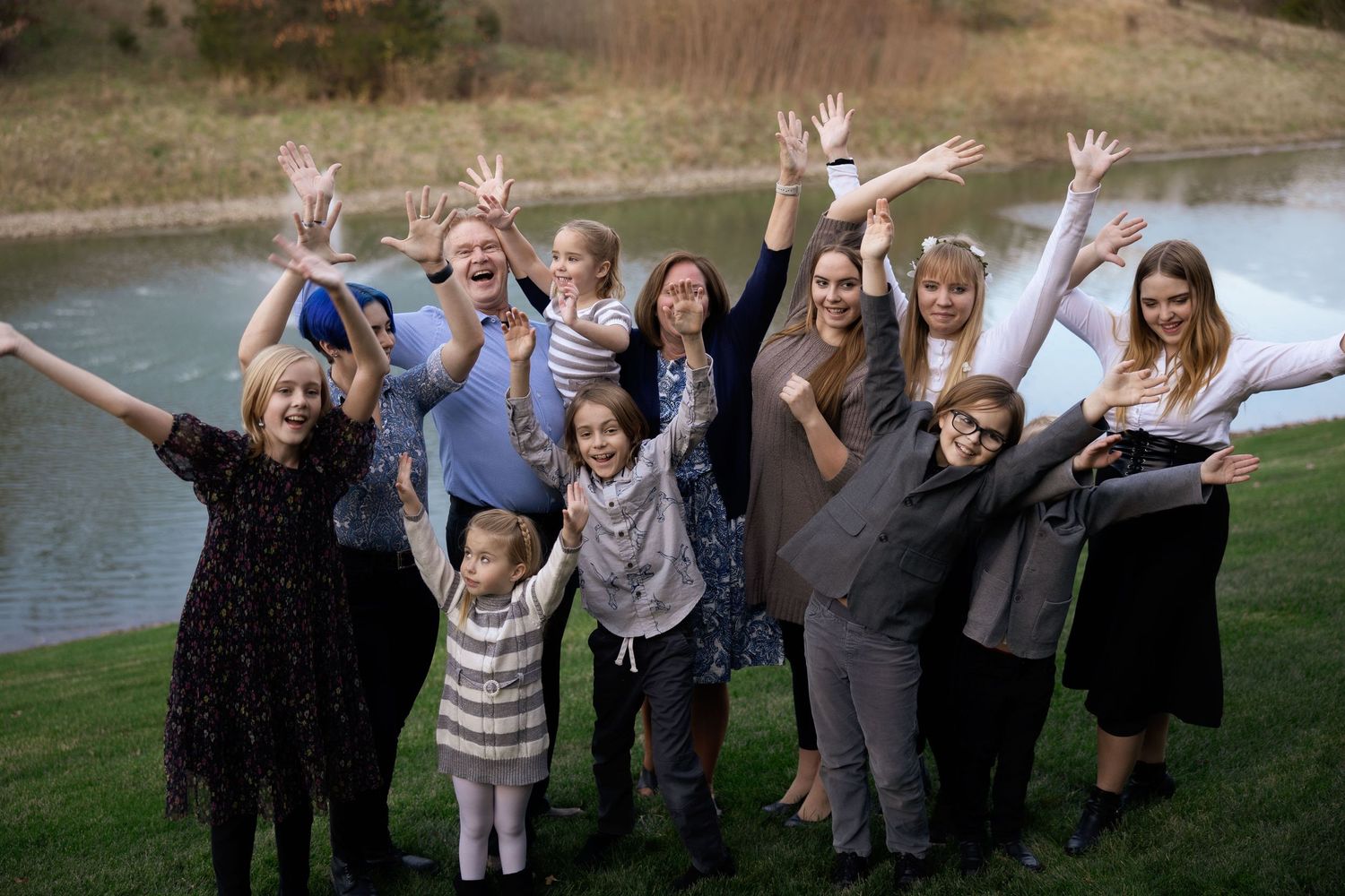 Group of people raising their hands joyfully by lakeside during outdoor gathering.