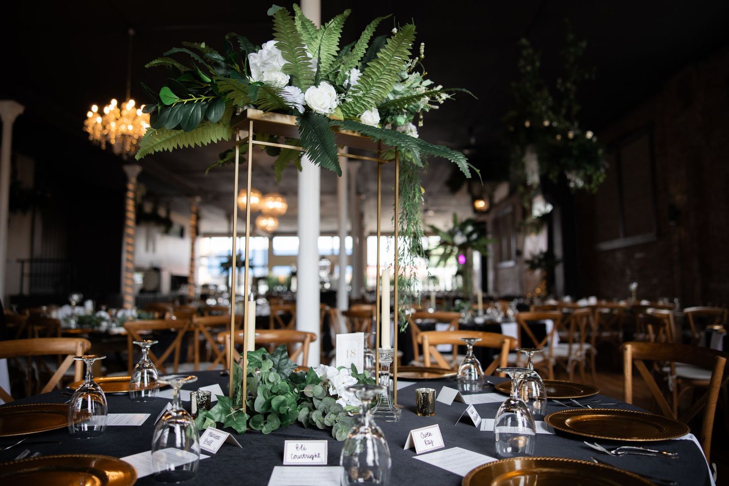 Modern wedding reception space with elegant greenery centerpieces and mood lighting.