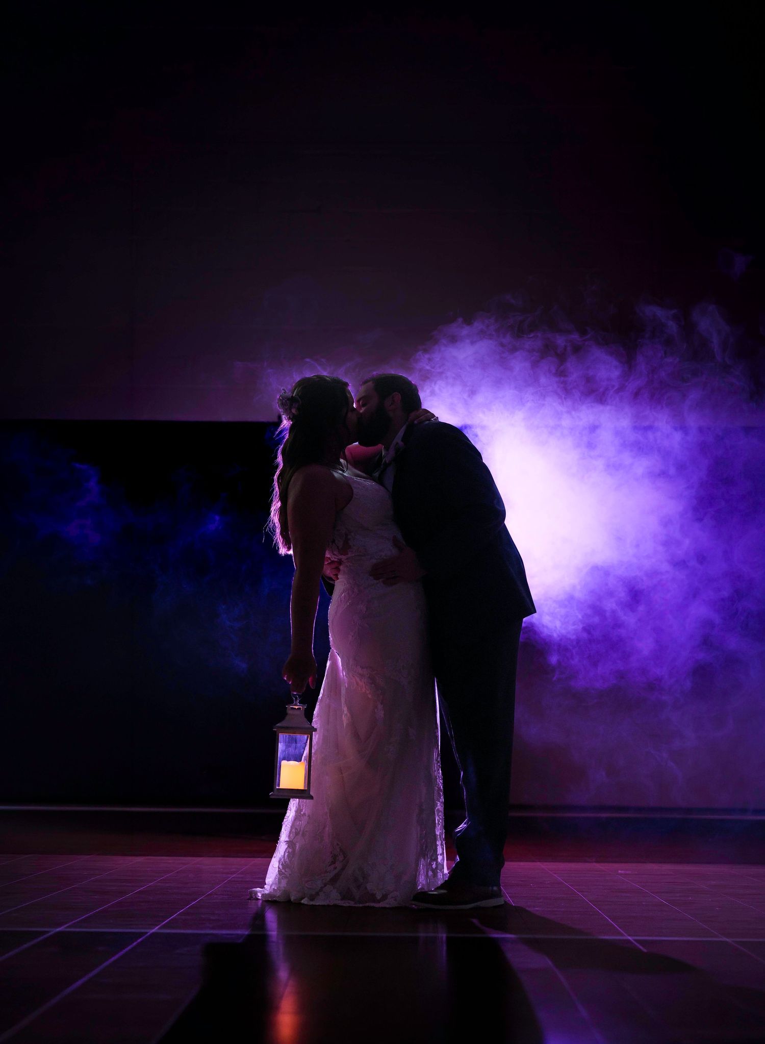 Bride and groom share a romantic kiss in dramatic purple smoke lighting, bride holding a glowing lantern.