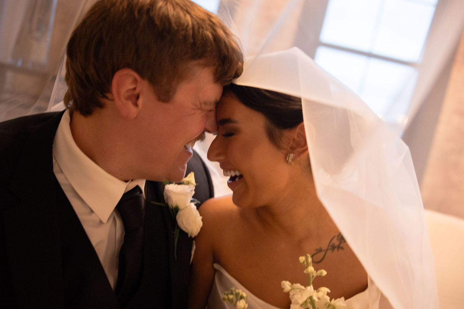 Romantic wedding moment captured in soft natural light by a window.