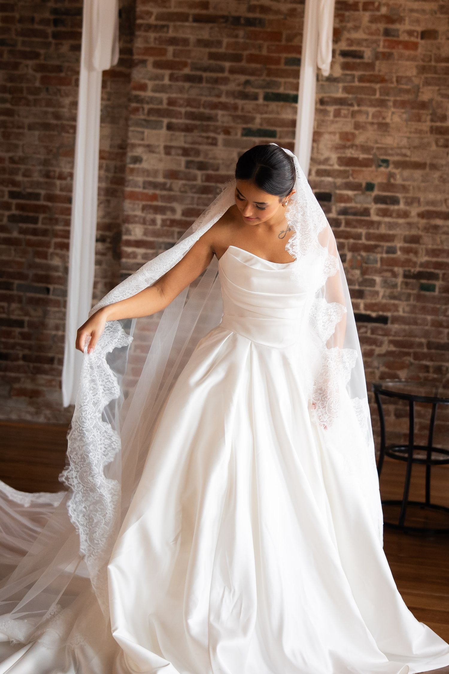 Bride in flowing white wedding dress twirling against exposed brick wall backdrop.