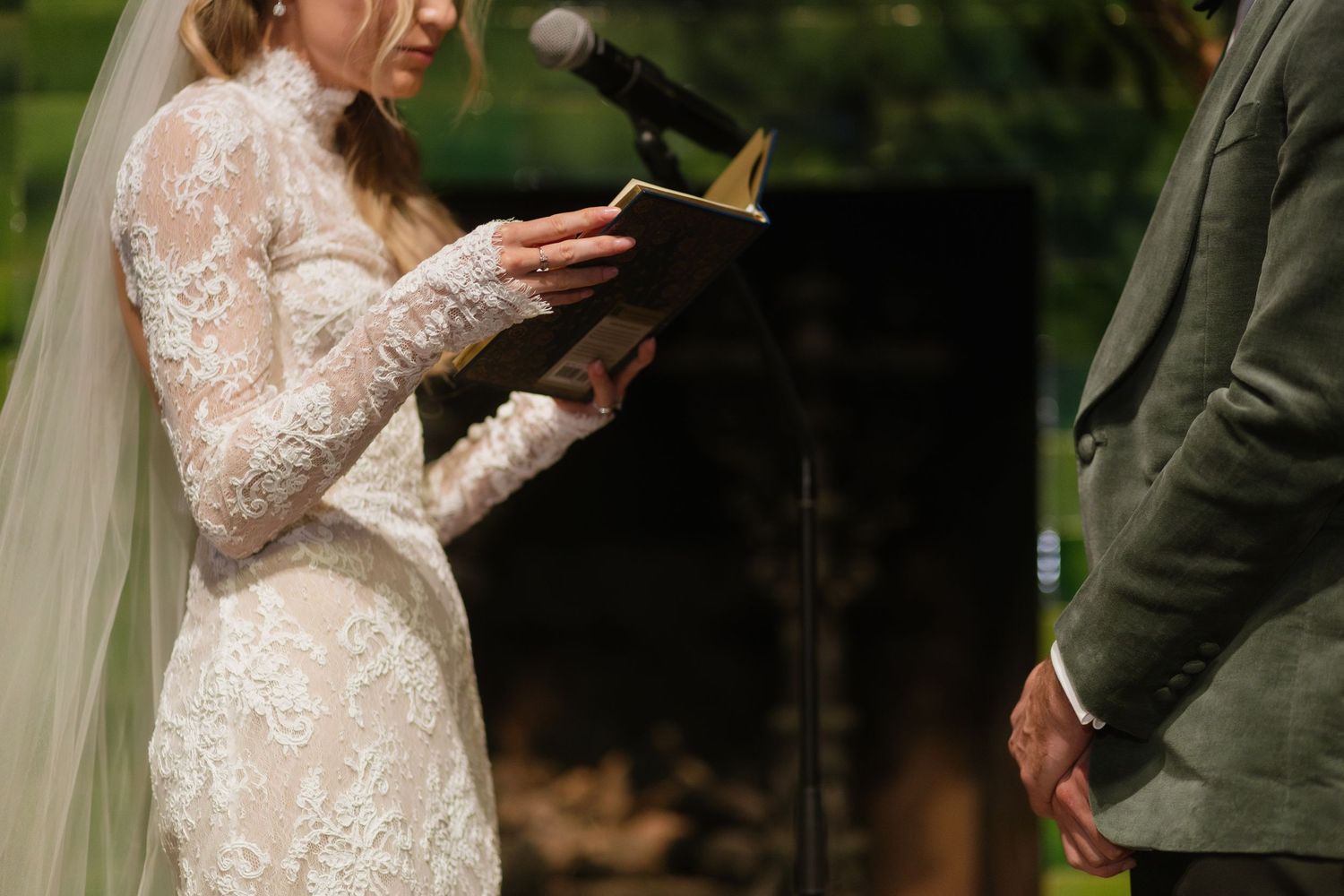 A couple exchanges vows during an outdoor wedding ceremony while holding hands in front of greenery.