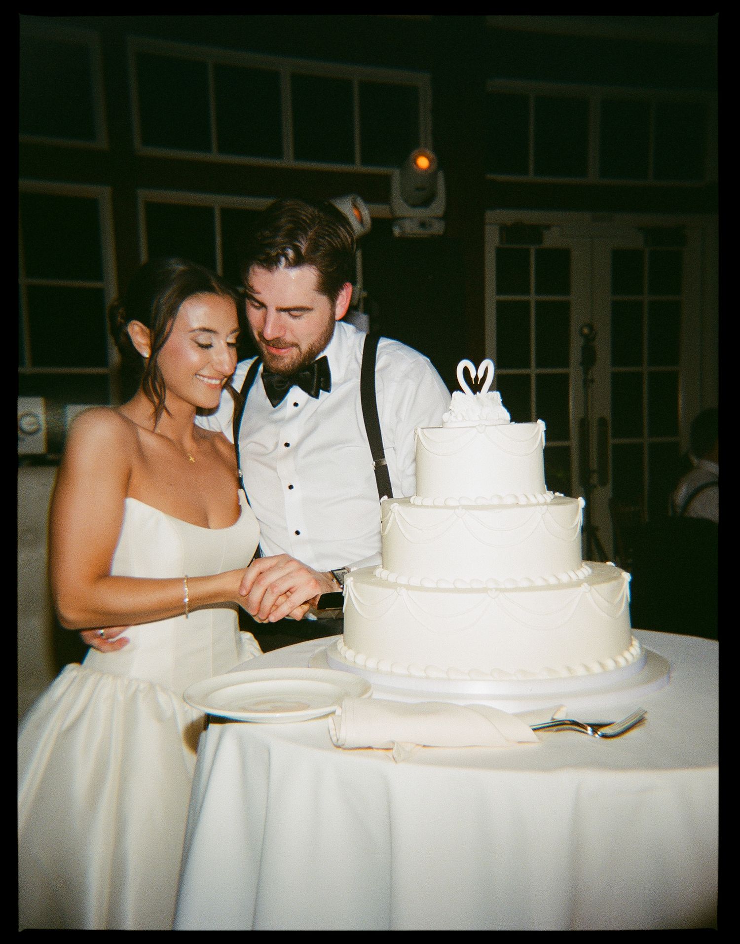Bride and groom cutting their three-tier white wedding cake together at their elegant reception venue.